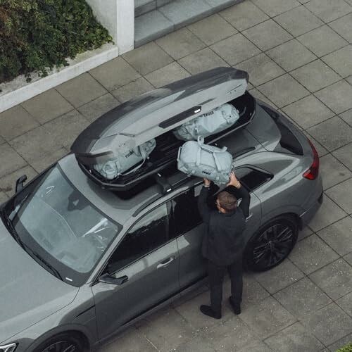 Person loading luggage into a car's rooftop cargo box.