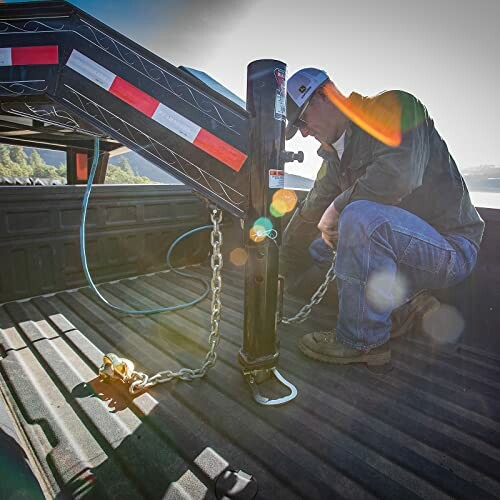 Person securing trailer hitch in truck bed with chains.